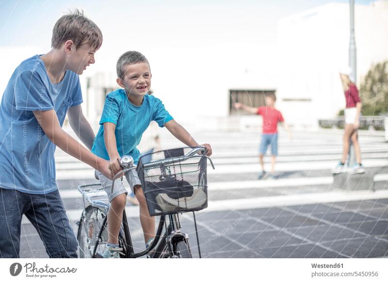 Junge bringt kleinem Bruder das Fahrradfahren bei Buben Knabe Jungen Knaben männlich lehren unterrichten beibringen Brüder fahrradfahren radeln lernen Bikes