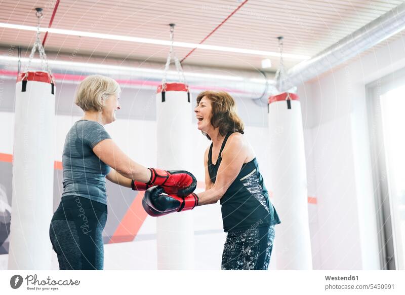 Zwei glückliche ältere Frauen mit Boxhandschuhen im Fitnessstudio trainieren Senioren alte Boxerin Boxerinnen Spaß Spass Späße spassig Spässe spaßig