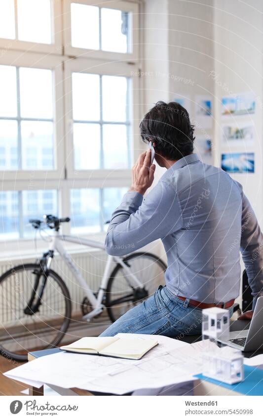 Mann benutzt Mobiltelefon im Büro Geschäftsmann Businessmann Businessmänner Geschäftsmänner telefonieren anrufen Anruf telephonieren Office Büros Fahrrad Bikes