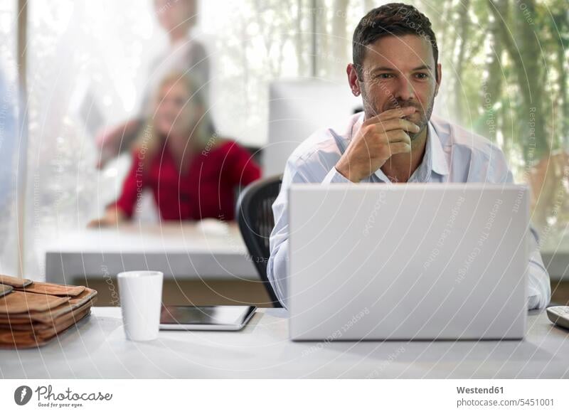 Junger Geschäftsmann sitzt im Büro und benutzt Laptop sitzen sitzend Schreibtisch Arbeitstisch Schreibtische Notebook Laptops Notebooks arbeiten glücklich Glück