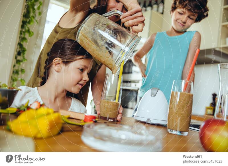 Mutter mit zwei Kindern gießt einen Smoothie in Gläser Mami Mutti Mütter Mama Smoothies Küche eingießen schütten einschenken schuetten Eltern Familie Familien