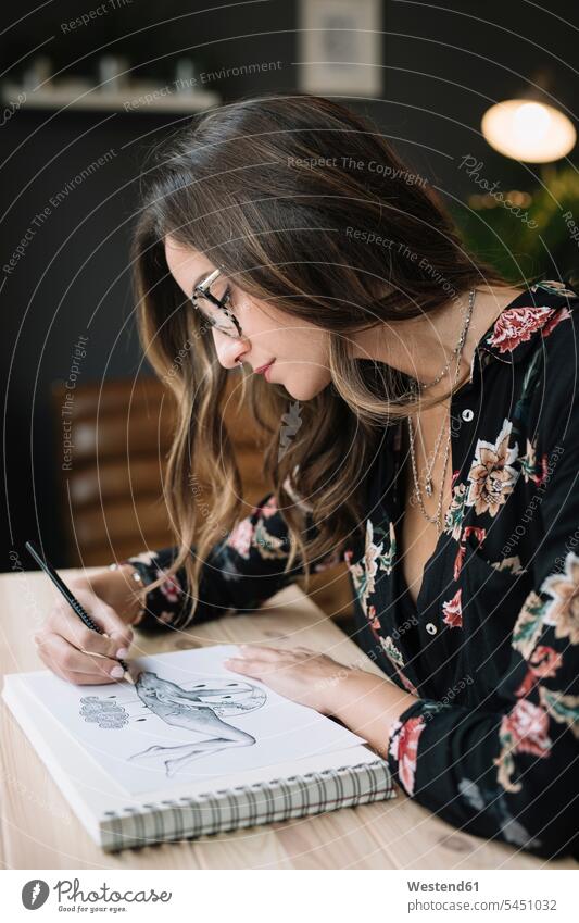 Porträt einer Frau, die im Skizzenbuch am Schreibtisch im Tätowierstudio zeichnet Portrait Porträts Portraits Arbeitstisch Schreibtische Skizzenbücher