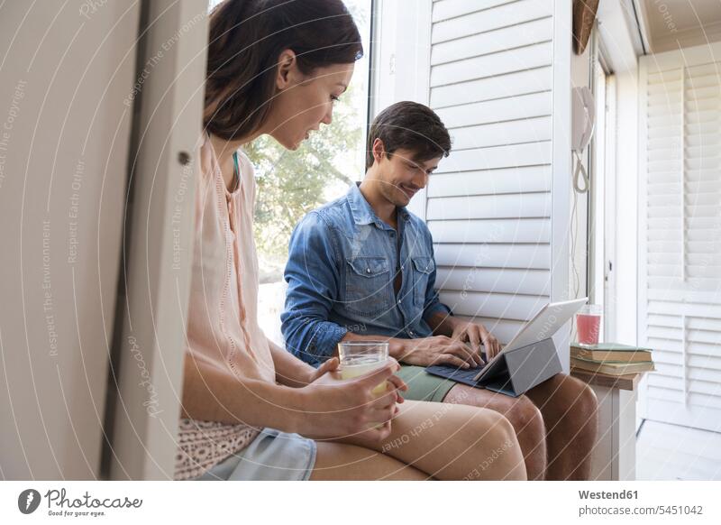 Junges Paar sitzt auf der Fensterbank mit Getränk und Tablette entspannt entspanntheit relaxt lächeln Pärchen Paare Partnerschaft sitzen sitzend Tablet Computer