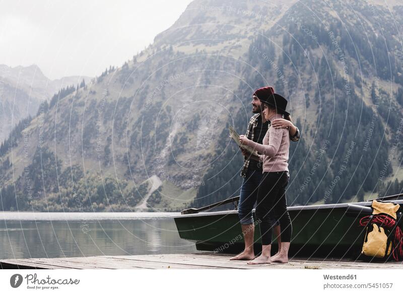 Österreich, Tirol, Alpen, Ehepaar mit Karte auf Steg am Bergsee stehend Paar Pärchen Paare Partnerschaft lächeln See Seen Mensch Menschen Leute People Personen