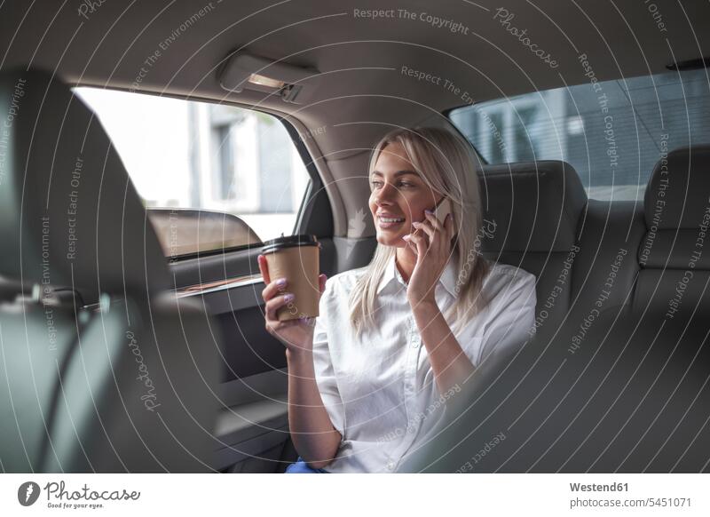 Lächelnde Geschäftsfrau mit Kaffee zum Mitnehmen auf dem Handy im Auto telefonieren anrufen Anruf telephonieren Wagen PKWs Automobil Autos lächeln Frau weiblich