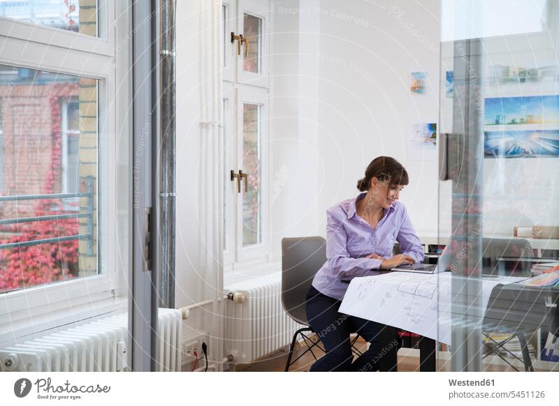 Lächelnde Frau mit Laptop im Büro Notebook Laptops Notebooks Office Büros Geschäftsfrau Geschäftsfrauen Businesswomen Businessfrauen Businesswoman Bauplan