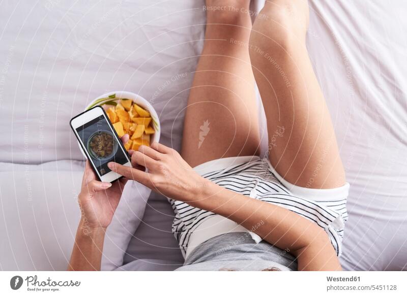 Nahaufnahme einer Frau, die eine Obstschale im Bett fotografiert Schüssel Schalen Schälchen Schüsseln Betten Früchte Handy Mobiltelefon Handies Handys