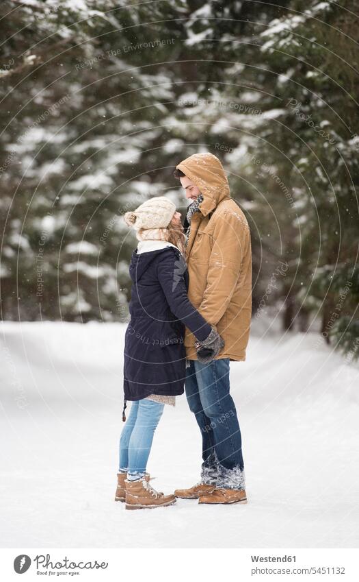 Glückliches junges Paar steht sich in schneebedeckter Winterlandschaft gegenüber Schnee Pärchen Paare Partnerschaft Wetter Mensch Menschen Leute People Personen