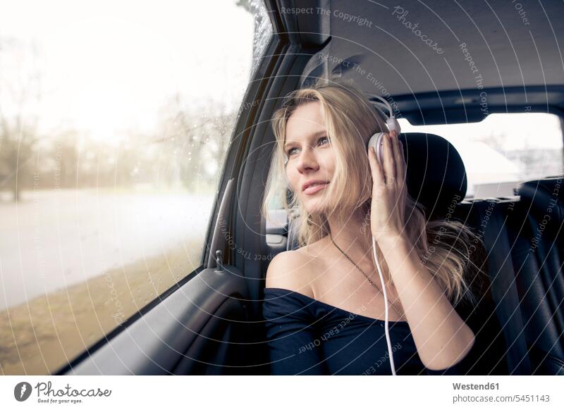 Porträt einer jungen Frau, die im Auto sitzt und mit Kopfhörern Musik hört Wagen PKWs Automobil Autos Kopfhoerer weiblich Frauen Kraftfahrzeug Verkehrsmittel
