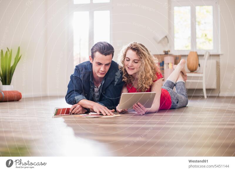 Junges Paar in neuer Wohnung auf dem Boden liegend mit Tablette zur Auswahl aus Farbmuster aussuchen auswählen Pärchen Paare Partnerschaft wohnen Wohnungen