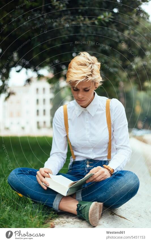 Teenager-Mädchen sitzt im Schneidersitz in einem Park und liest ein Buch sitzen hip lernen blond Teenagerin Mensch Wissen Bildung Boden lesen Erwachsen werden
