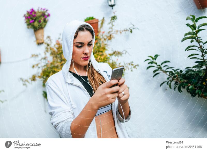 Junge Frau trägt Kopfhörer und schreibt eine Textnachricht Smartphone iPhone Smartphones Musik hören Kopfhoerer lesen Lektüre SMS besorgt Sorgen jung weiblich