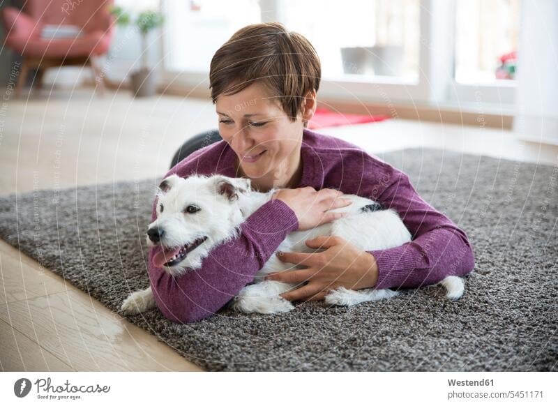 Frau liegt auf Teppich im Wohnzimmer und umarmt ihren Hund Hunde weiblich Frauen Haustier Haustiere Tier Tierwelt Tiere Erwachsener erwachsen Mensch Menschen