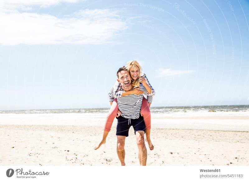 Glückliches, verspieltes Paar am Strand lachen Huckepack Beach Straende Strände Beaches Pärchen Paare Partnerschaft positiv Emotion Gefühl Empfindung Emotionen