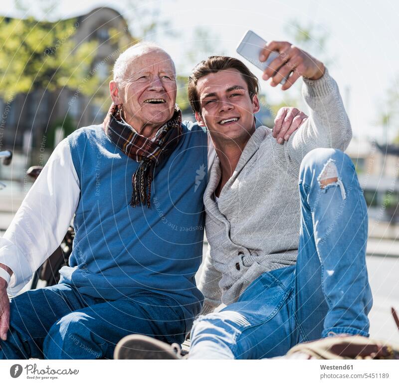 Älterer Mann und erwachsener Enkel auf einer Bank machen ein Selfie Spaß Spass Späße spassig Spässe spaßig glücklich Glück glücklich sein glücklichsein sitzen