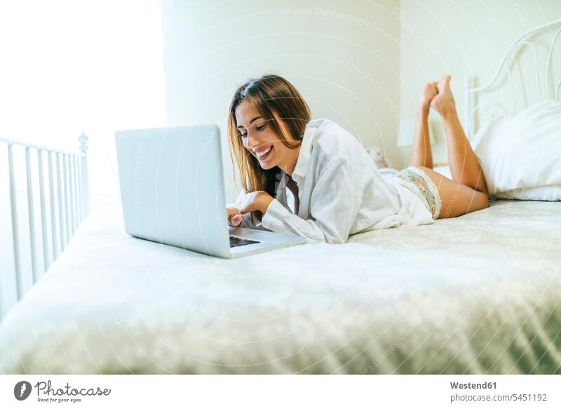 Lächelnde Frau, die mit einem Laptop auf dem Bett liegt Betten Notebook Laptops Notebooks weiblich Frauen Computer Rechner Erwachsener erwachsen Mensch Menschen