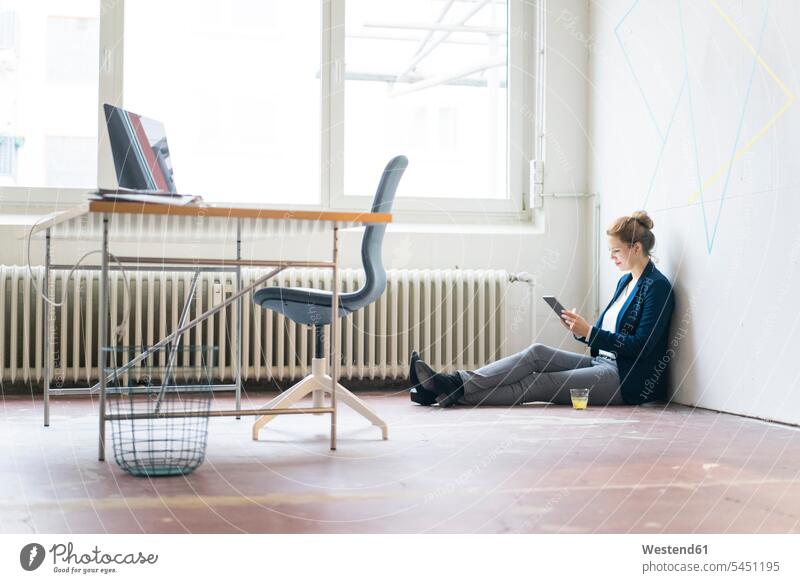 Geschäftsfrau, die im Büro auf dem Boden sitzt und ein digitales Tablet benutzt sitzen sitzend arbeiten Arbeit Office Büros Internet Geschäftsfrauen