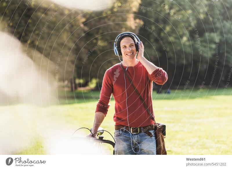 Lachender Mann mit Rennrad, der in einem Park mit Kopfhörern Musik hört Männer männlich Kopfhoerer Parkanlagen Parks Erwachsener erwachsen Mensch Menschen Leute