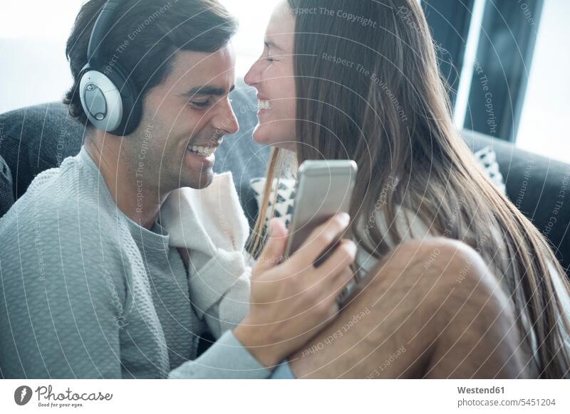 Glückliches junges Paar mit Kopfhörern und Smartphone zu Hause Pärchen Paare Partnerschaft entspannt entspanntheit relaxt Kopfhoerer glücklich glücklich sein