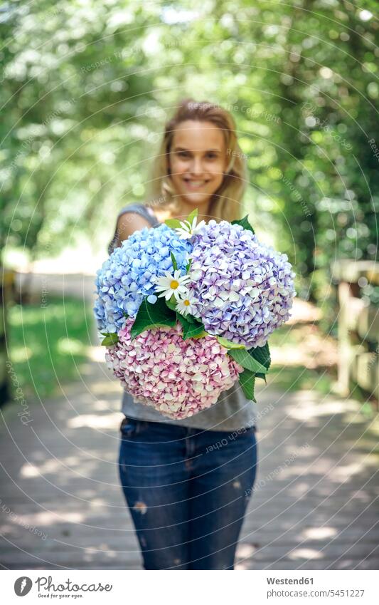 Lächelnde junge Frau zeigt einen Strauss Hortensien und Gänseblümchen zeigen vorführen präsentieren Vorführung herzeigen lächeln Blume Blumen Blüte Blumenstrauß
