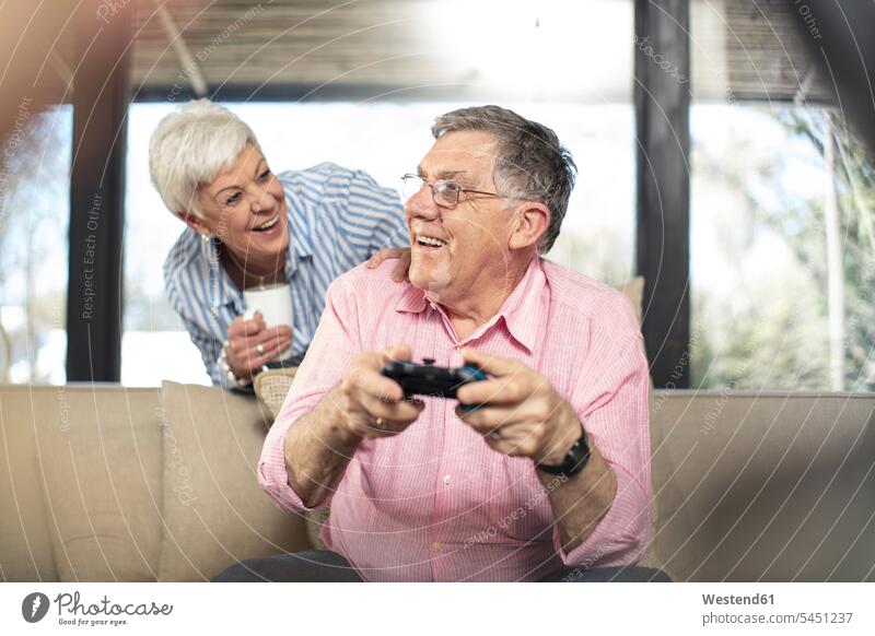 Glücklicher älterer Mann mit Frau spielt zu Hause auf der Couch Videospiel Sofa Couches Liege Sofas Zuhause daheim glücklich glücklich sein glücklichsein
