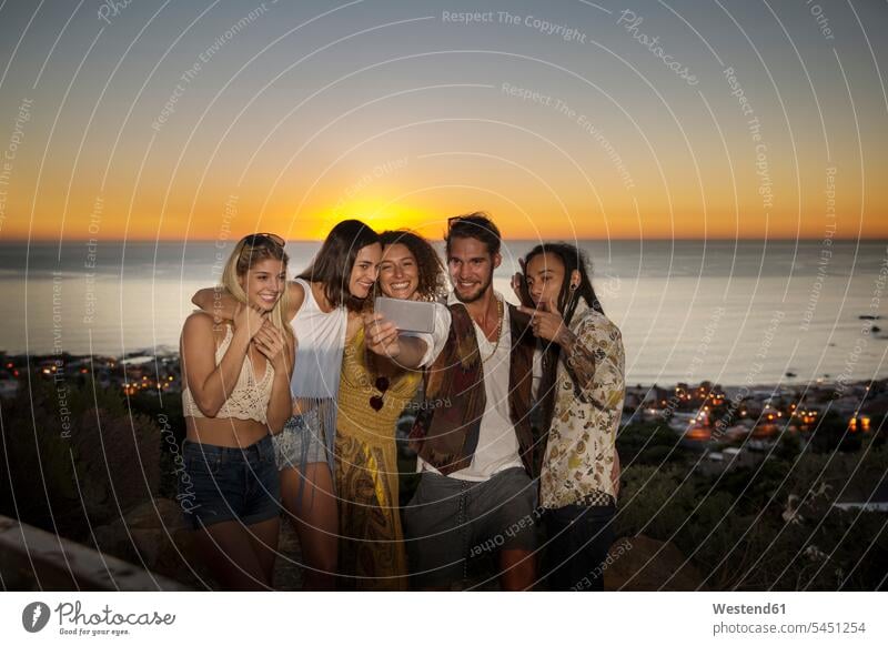Junge Leute machen ein Selfie an der Küste bei Sonnenuntergang Kueste Kuesten Küsten Selfies Freunde Spaß Spass Späße spassig Spässe spaßig Freundschaft