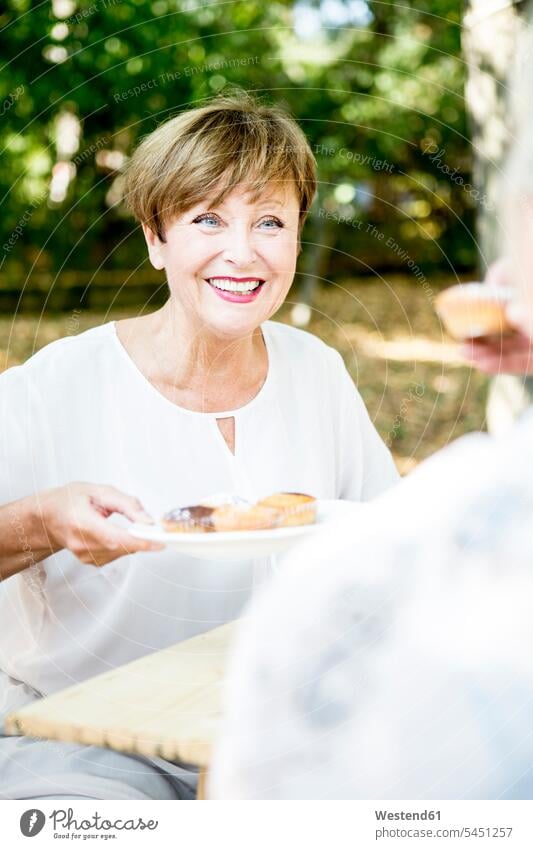 Lächelnde ältere Frau bietet Muffins an Seniorin Seniorinnen alt weiblich Frauen lächeln anbieten Senioren Erwachsener erwachsen Mensch Menschen Leute People