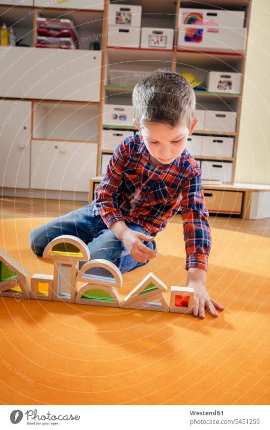 Junge stellt Holzspielzeugformen auf Teppich im Kindergarten auf Kids Buben Knabe Jungen Knaben männlich Kindergaerten Kindergärten spielen Mensch Menschen
