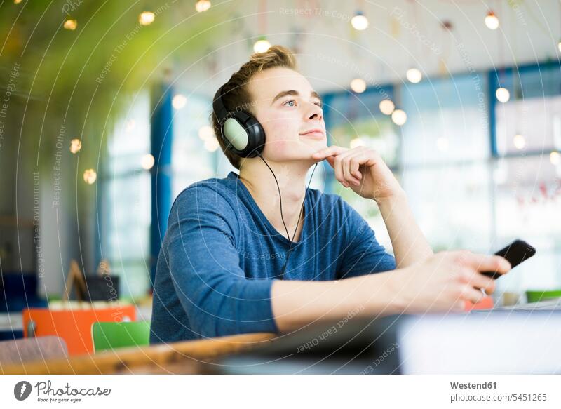 Porträt eines jungen Mannes, der in einem Café mit Kopfhörern Musik hört Kopfhoerer Student Hochschueler Studierender Hochschüler Studenten Portrait Porträts