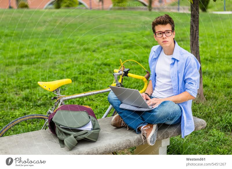 Nachdenklicher junger Mann mit Rennrad, der mit einem Laptop auf einer Bank sitzt Männer männlich Notebook Laptops Notebooks Erwachsener erwachsen Mensch