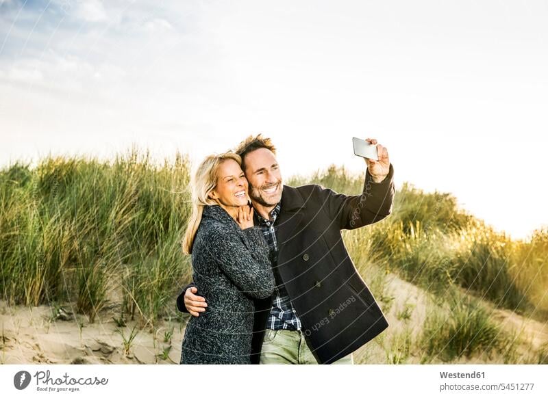 Glückliches Paar in den Dünen macht ein Selfie Pärchen Paare Partnerschaft Strand Beach Straende Strände Beaches Selfies Handy Mobiltelefon Handies Handys
