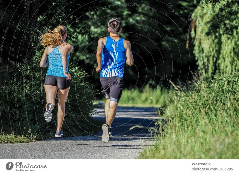 Rückenansicht eines jungen Paares beim Joggen im Park Jogging Pärchen Partnerschaft Fitness fit Gesundheit gesund Sport Mensch Menschen Leute People Personen