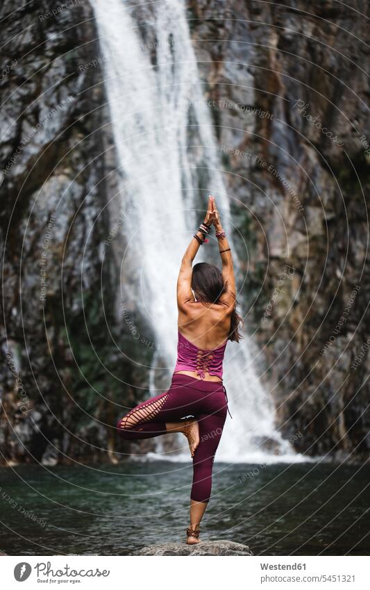 Italien, Lecco, Frau macht Baum-Yoga-Pose auf einem Felsen in der Nähe eines Wasserfalls Wasserfälle Wasserfaelle Yoga-Übungen Yogauebungen Yogaübungen
