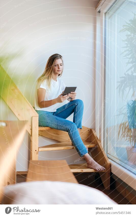 Junge Frau sitzt zu Hause und benutzt ein digitales Tablett Treppe Treppenaufgang lesen Lektüre sitzen sitzend Zuhause daheim Gemütlich Wohlfühlen behaglich