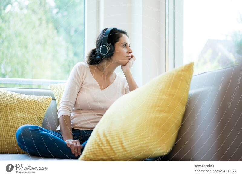 Frau sitzt allein auf dem Sofa und hört Musik mit Kopfhörern Musik hören sitzen sitzend Allein alleine einzeln Kopfhoerer Couches Liege Sofas Textfreiraum Ruhe