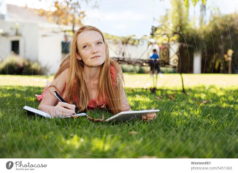 Grl mit langen roten Haaren im Gras liegend mit Tablette und Notizbuch liegt Tablet Computer Tablet-PC Tablet PC iPad Tablet-Computer Mädchen weiblich entspannt