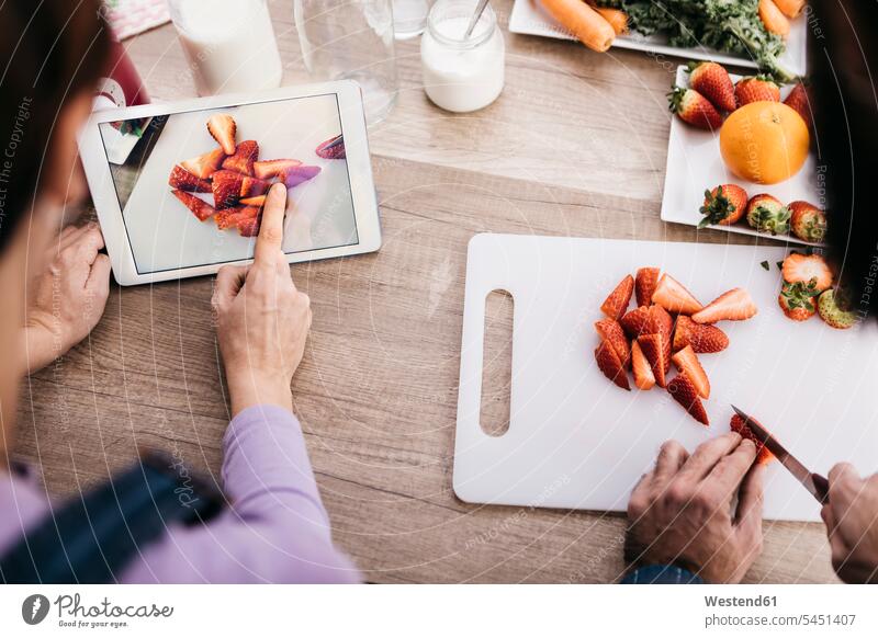 Frau, die mit Tablette fotografiert, während ihr Freund Erdbeeren schneidet, Teilansicht Tablet Computer Tablet-PC Tablet PC iPad Tablet-Computer fotografieren