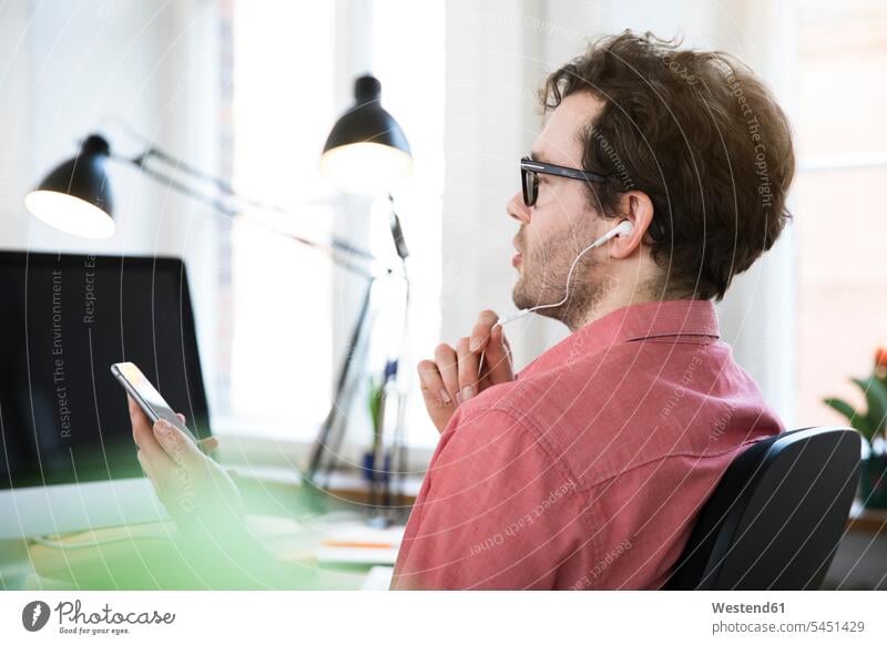 Mann mit Kopfhörern mit Mobiltelefon im Büro Office Büros Arbeitsplatz Arbeitsstätte Arbeitstelle Handy Handies Handys Mobiltelefone arbeiten Männer männlich
