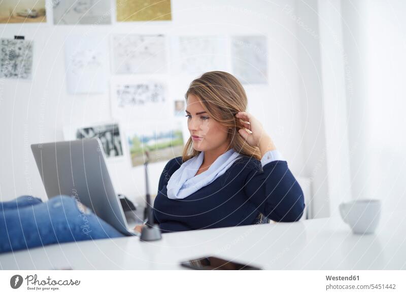 Junge Frau mit Laptop am Schreibtisch im Büro arbeiten Arbeit Europäerin Europäerinnen Kaukasierin Kaukasierinnen Online Office Büros betrachten betrachtend