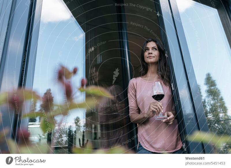 Frau hält ein Glas Rotwein und schaut aus dem Fenster entspannt entspanntheit relaxt weiblich Frauen Rotweine Entspannung relaxen entspannen Erwachsener