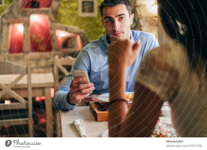 Mann mit Handy von Angesicht zu Angesicht mit seiner Freundin in einem Restaurant Smartphone iPhone Smartphones Lokal Speiserestaurant Lokale Speiselokale