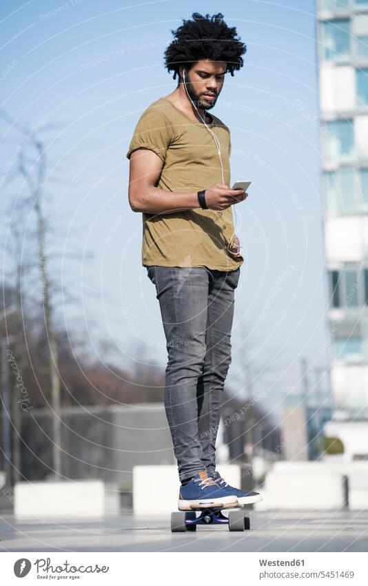 Junger Mann fährt Longboard im Skatepark und schaut auf sein Smartphone Skateboard Rollbretter Skateboards Männer männlich fahren Erwachsener erwachsen Mensch