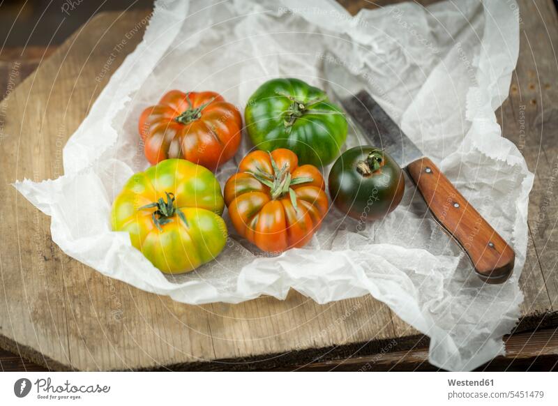 Fünf verschiedene Ochsenherz-Tomaten und Messer auf Papier Niemand Variation Abweichung Variationen Ochsenherztomate Ochsenherztomaten Gemüse Gemuese roh