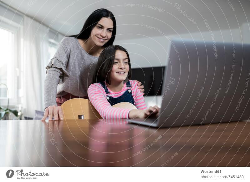 Mutter und Tochter lächelnd vor dem Laptop, die Tochter hält eine Gitarre Mami Mutti Mütter Mama Notebook Laptops Notebooks Gitarren Töchter Eltern Familie