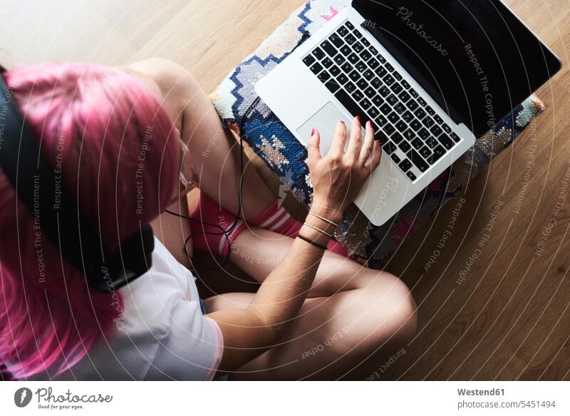 Junge Frau mit rosa Haaren trägt Kopfhörer und benutzt zu Hause einen Laptop Notebook Laptops Notebooks Kopfhoerer weiblich Frauen Computer Rechner Erwachsener