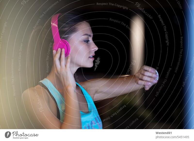 Junge Frau mit rosa Kopfhörern bei der Kontrolle ihrer Smartwatch trainieren telefonieren anrufen Anruf telephonieren Kopfhoerer Musik hören checken Joggerin