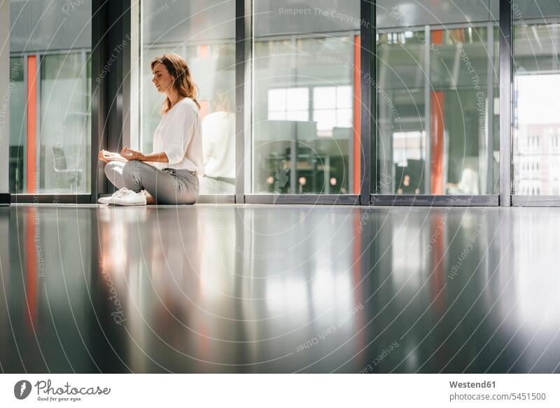 Geschäftsfrau, die im Büro Yoga praktiziert, meditiert üben ausüben Übung trainieren sitzen sitzend sitzt auf dem Boden sitzen auf dem Boden sitzend