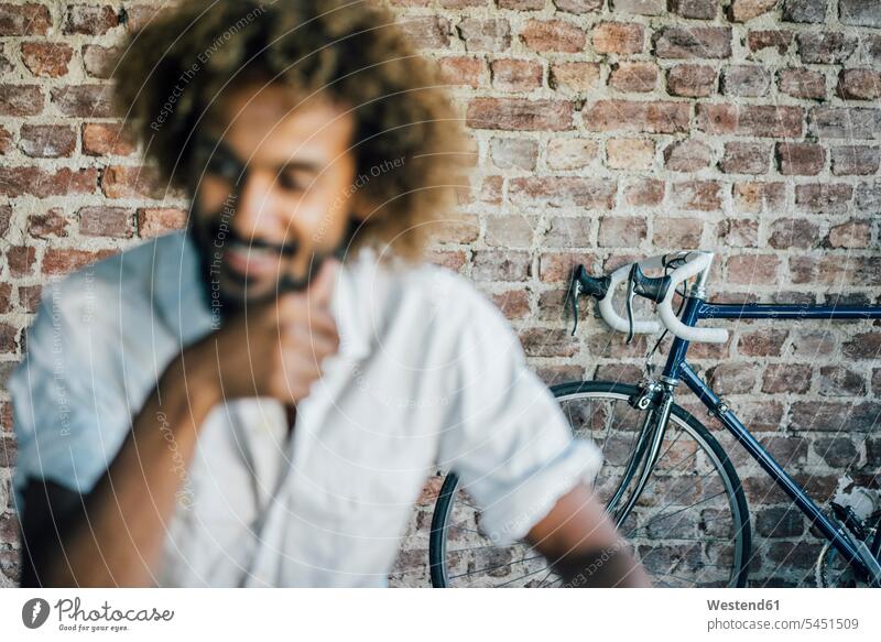 Lächelnder junger Mann mit Fahrrad im Hintergrund lächeln Männer männlich Bikes Fahrräder Räder Rad Erwachsener erwachsen Mensch Menschen Leute People Personen