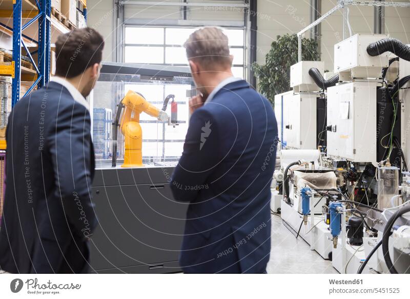 Zwei Geschäftsleute in Fabrikhalle mit Blick auf Industrieroboter Kollegen Arbeitskollegen Mann Männer männlich Fabriken ansehen Erwachsener erwachsen Mensch