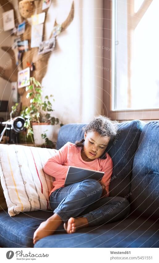 Kleines Mädchen am Sitztablett, auf dem Sofa sitzend Couches Liege Sofas weiblich Allein alleine einzeln Zuhause zu Hause daheim Tablet Tablet Computer
